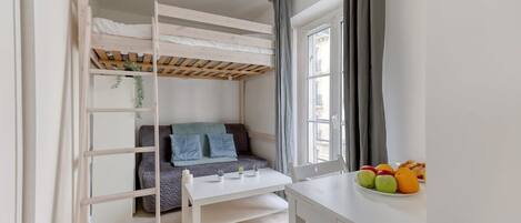 Une pièce avec un lit superposé, une petite table, un canapé et une fenêtre avec des rideaux.
