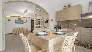 Comedor con una mesa preparada para cuatro personas, rodeado de sillas, en una cocina moderna con armarios y horno empotrado.