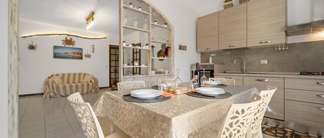 Uma área de refeições com uma mesa posta para quatro pessoas, cercada por cadeiras, em uma cozinha moderna com armários e forno embutido.
