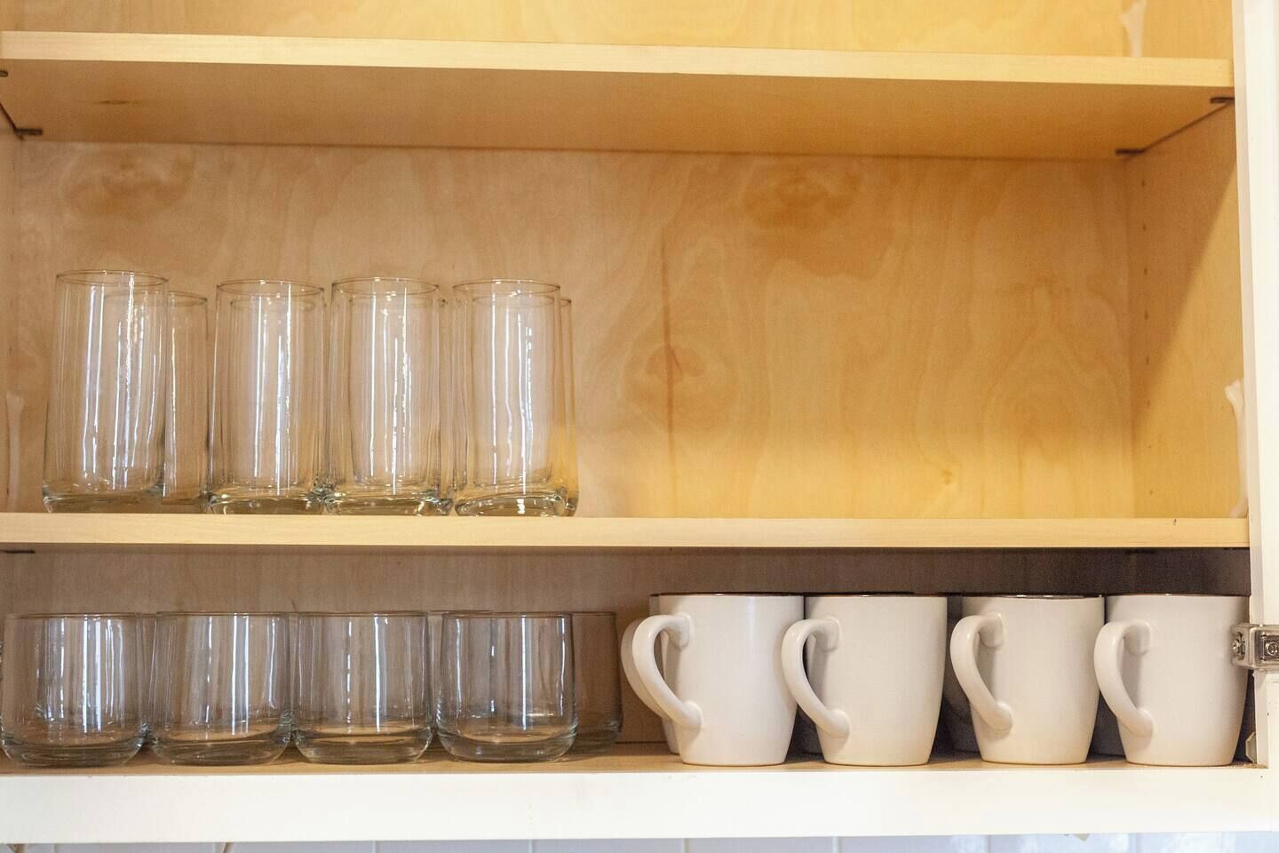 A shelf with clear glass tumblers and white ceramic mugs.