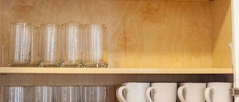 A shelf with clear glass tumblers and white ceramic mugs.
