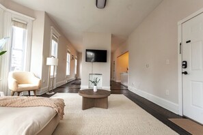 Ein Hotelzimmer mit einem Bett, einem runden Couchtisch, einem Sessel, einem an der Wand befestigten Fernseher und einer Tür mit Sicherheitsschloss.