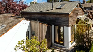 A modern house with a sloped roof, a chimney, and a small attached structure with large windows. - Pear Tree Cottage - pet friendly (Oxfordshire)