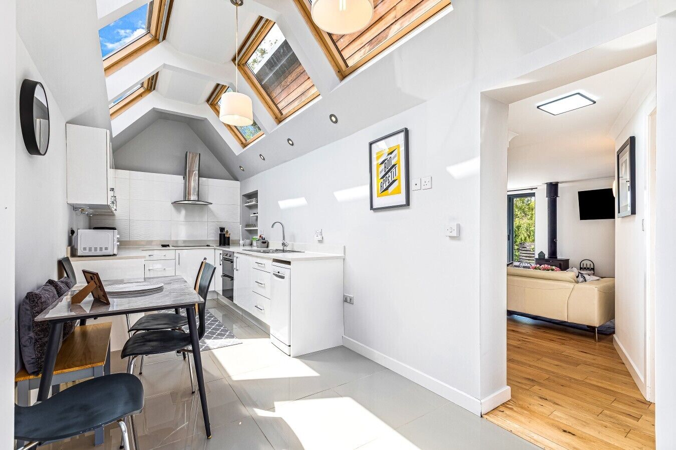 Eine moderne Küche mit Dachfenstern, ein Essbereich mit Tisch und Stühlen sowie eine Wohnbereich mit Sofa und Kamin.