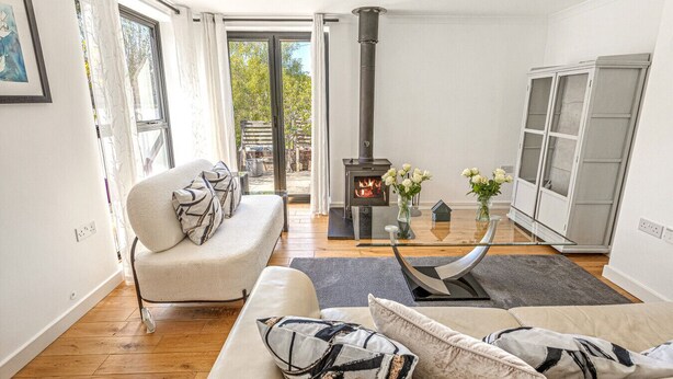 A living room with a sofa, a glass coffee table, a fireplace, and a view through a glass door. - Pear Tree Cottage - pet friendly (Oxfordshire)