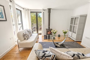 A living room with a sofa, a glass coffee table, a fireplace, and a view through a glass door. - Pear Tree Cottage - pet friendly (Oxfordshire)