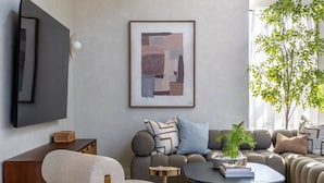Ein modernes Wohnzimmer mit einer Sofagarnitur, einem Couchtisch, einem Sessel, einem an der Wand befestigten Fernseher und einem gerahmten abstrakten Gemälde.