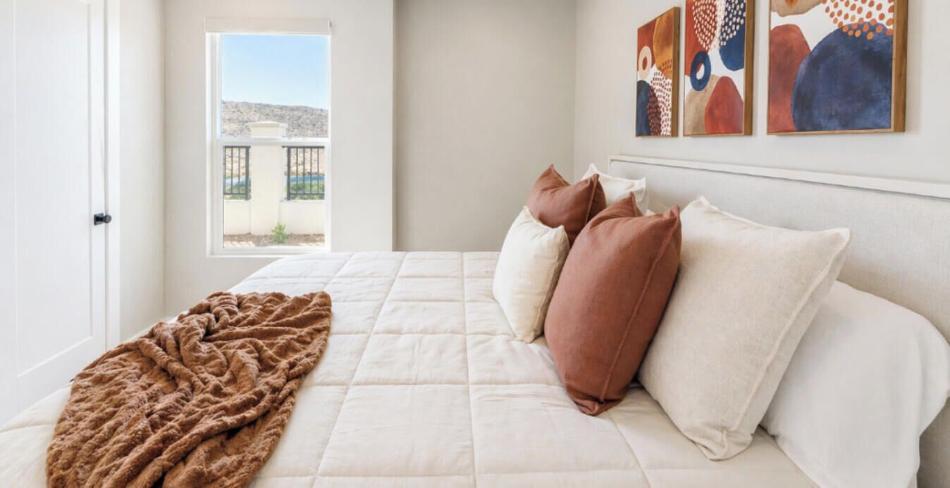 Un letto con una coperta, cuscini e una trapunta in una stanza con una finestra e opere d'arte astratte alle pareti.