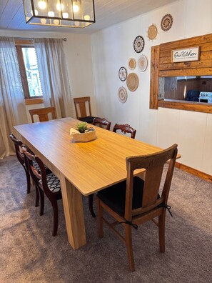 A dining area with a wooden table, six chairs, a hanging light fixture, and a wall-mounted sign.
