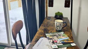 Une table en bois, surmontée d’une suspension noire, avec une plante en pot, une tasse et des magazines.