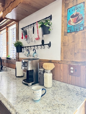 A kitchen with a coffee maker, jars, a mug, and a sign saying 'Coffee and Friends Make the Perfect Blend'.