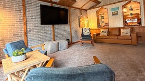 Un salon chaleureux avec un mur en briques, un téléviseur à écran plat, des meubles en bois et un ventilateur de plafond.