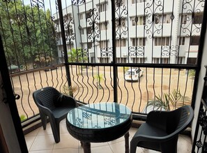 Een balkon met een glazen tafel en twee stoelen, met uitzicht op een woongebied waar een witte auto op straat geparkeerd staat.