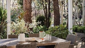 An outdoor patio with a round table and wicker chairs, surrounded by greenery and trees. - Scribbly Gums Berrara (Berrara)