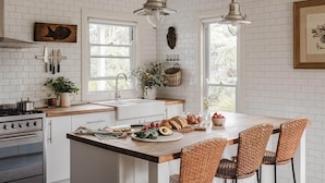 A kitchen with a central island, wooden chairs, a stove, and hanging kitchen utensils. - Scribbly Gums Berrara (Berrara)