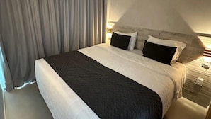 Hotellihuone, jossa on suuri sänky, sängynpääty, yöpöytä ja verho.
