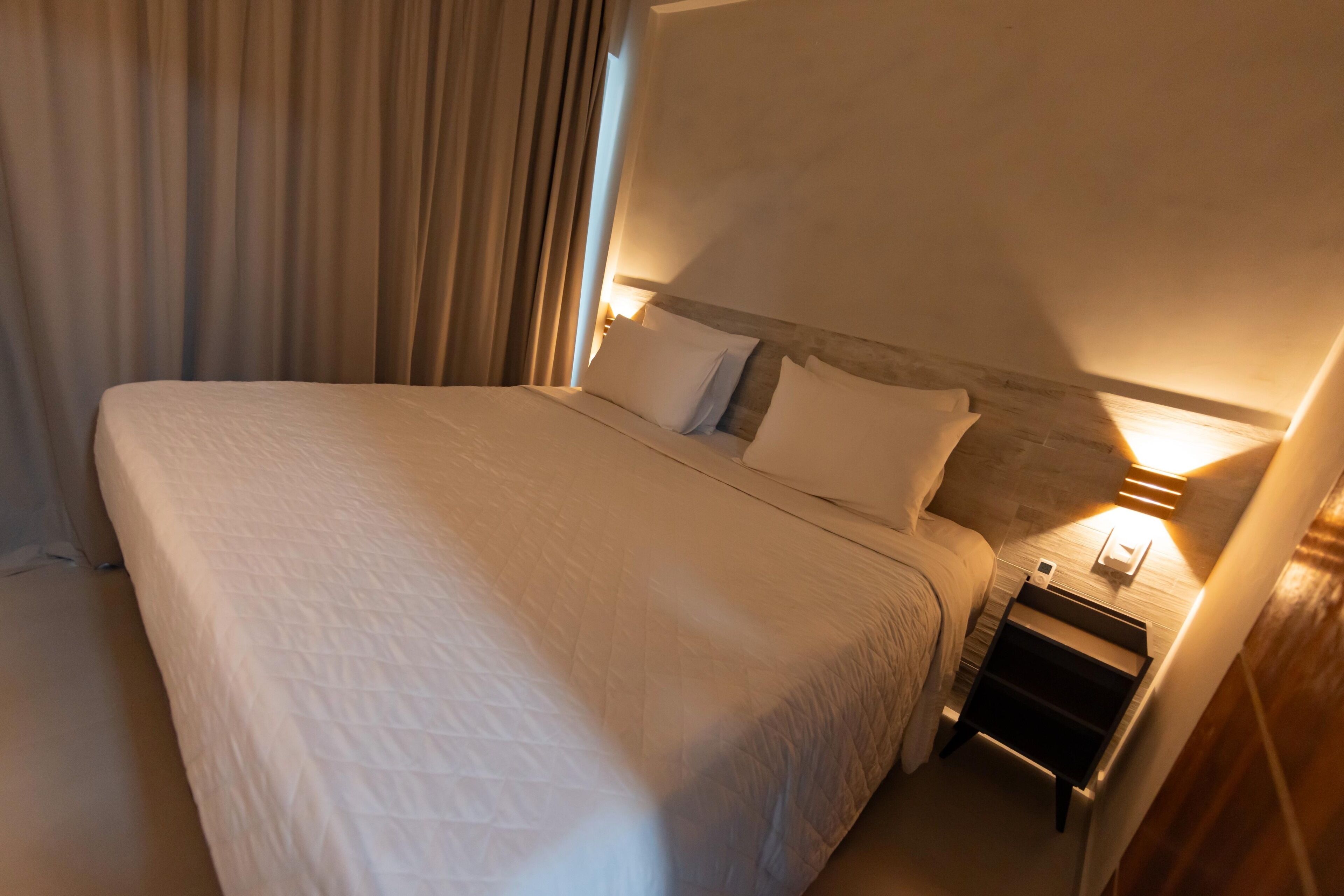 A neatly made bed with a quilted cover, a bedside table with a lamp, and a wooden headboard.