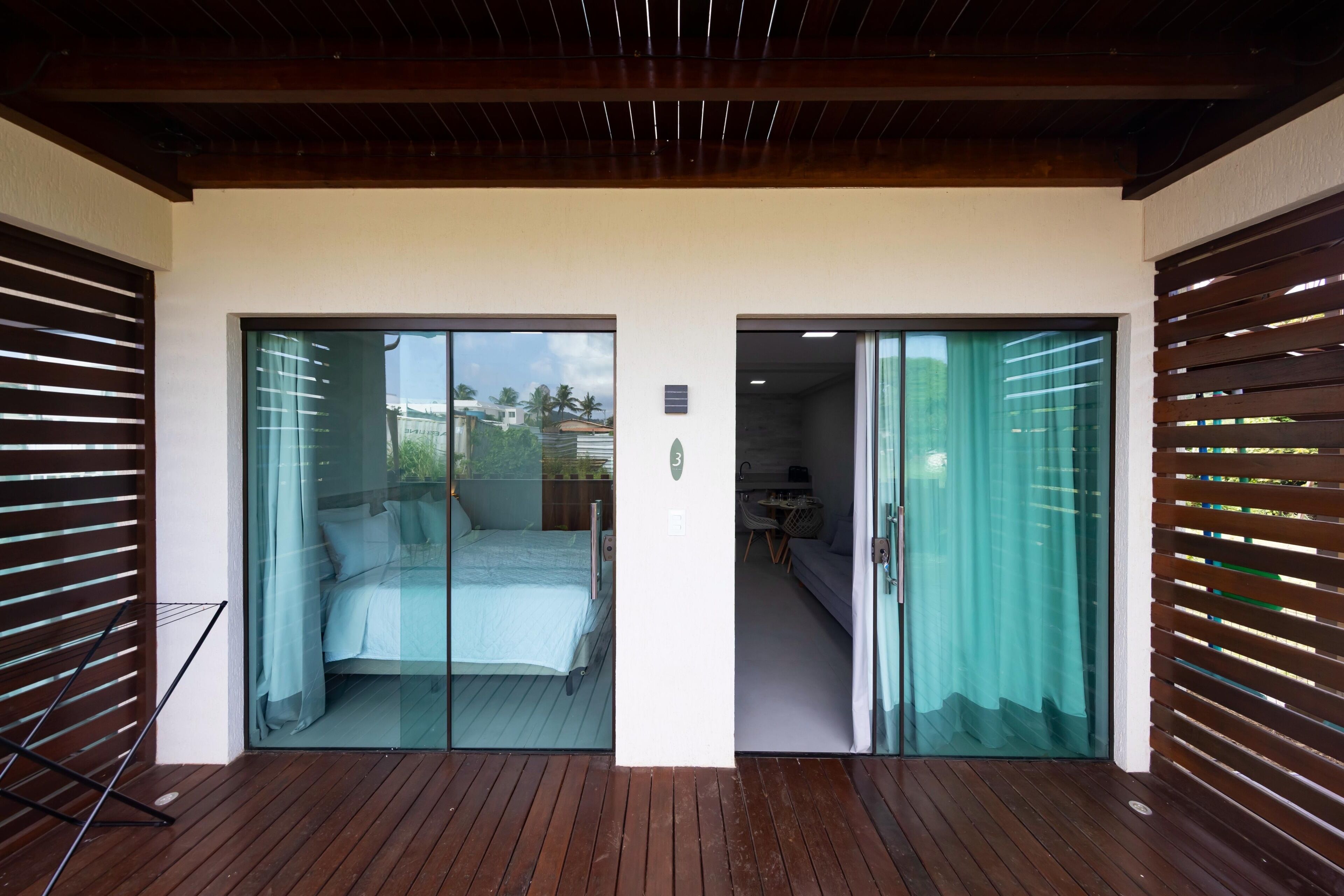 Quarto moderno com uma cama, uma mesinha e uma cadeira. Há uma porta de correr de vidro que dá para outro quarto.