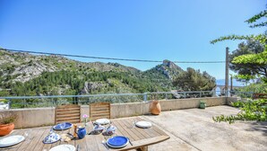 Ein Holztisch im Freien mit Tellern, Gläsern und Besteck, mit Blick auf eine Berglandschaft.
