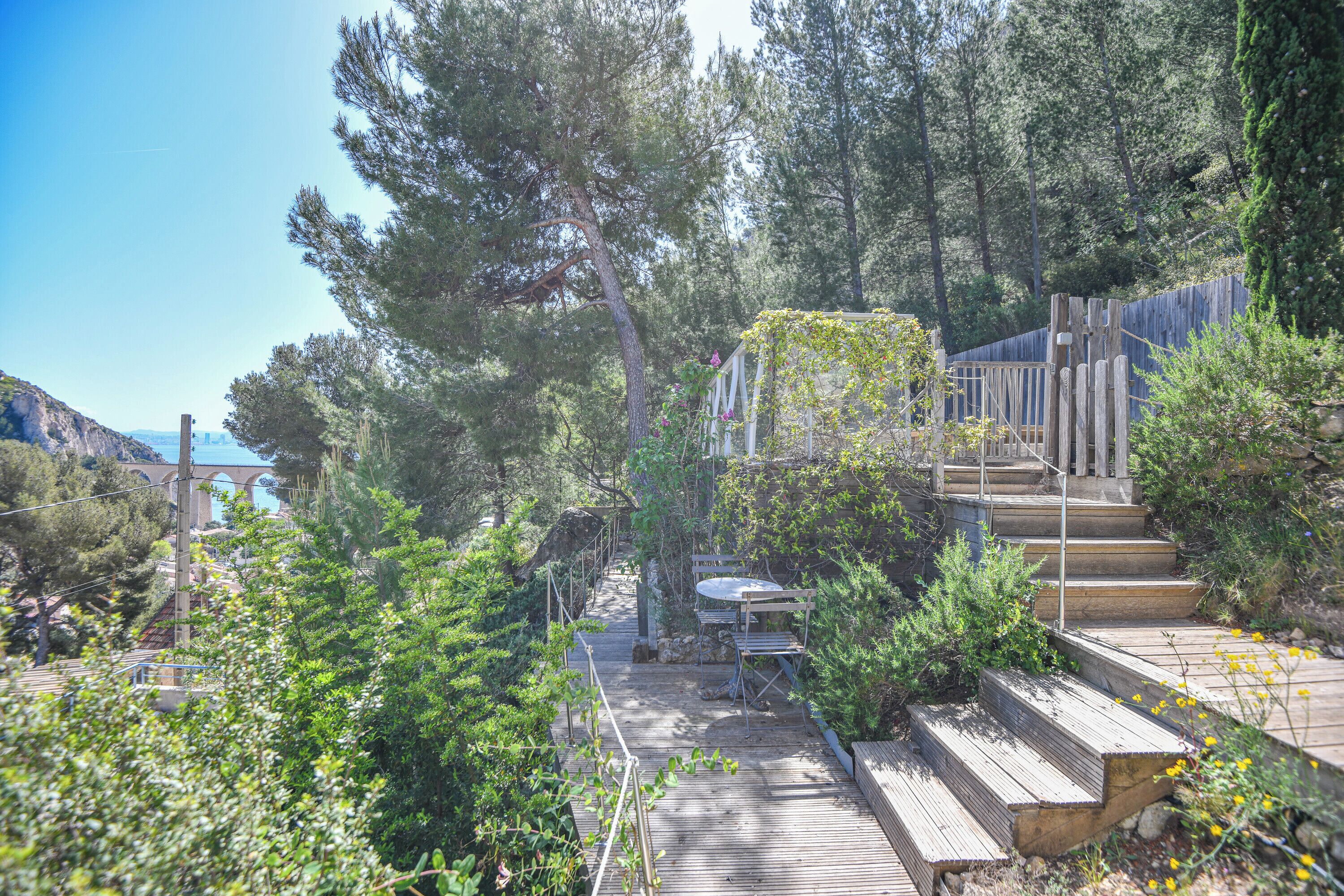 A wooden deck with a table and chairs, surrounded by greenery and a wooden fence.