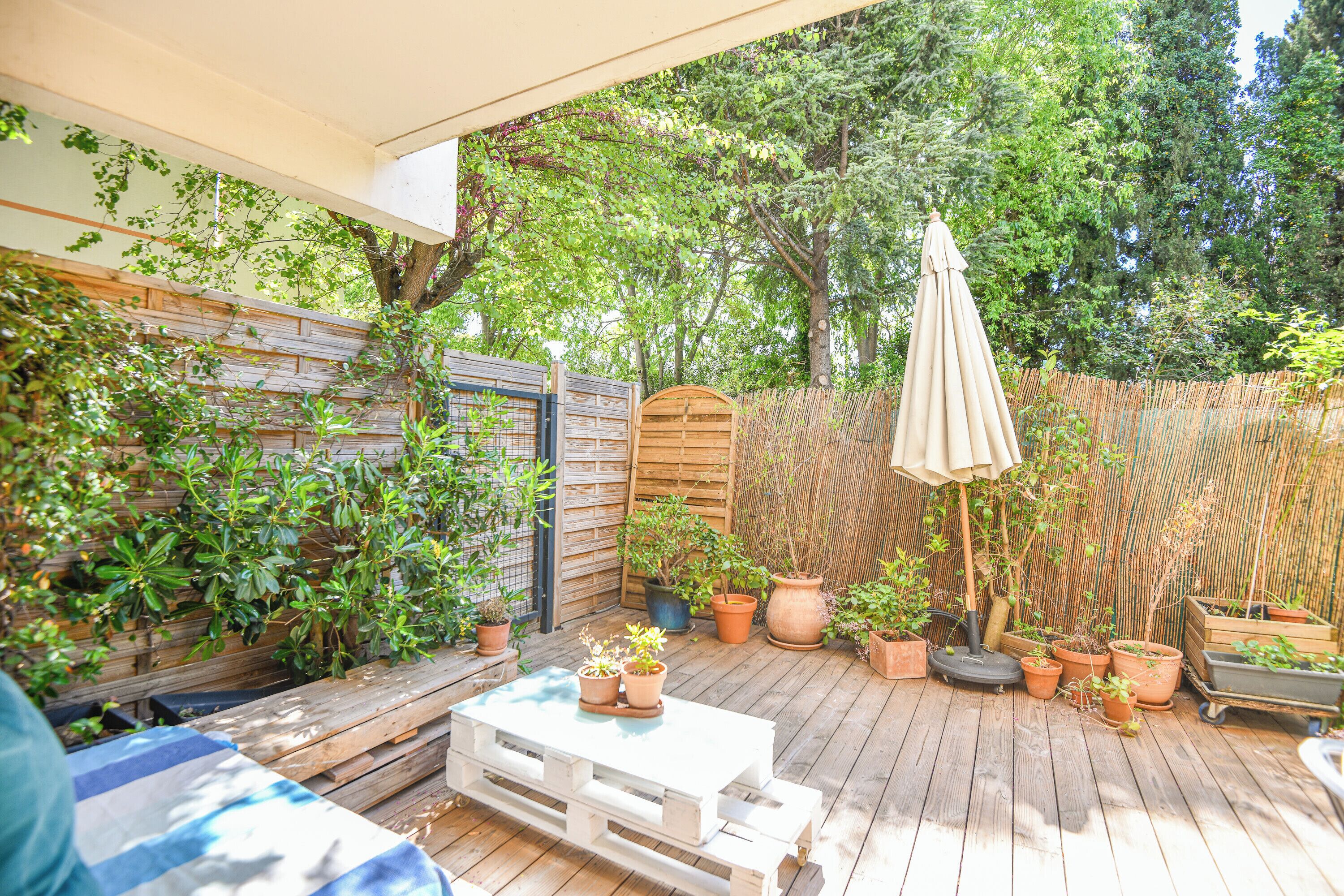 A wooden deck with a white table and benches, surrounded by potted plants and a bamboo fence.