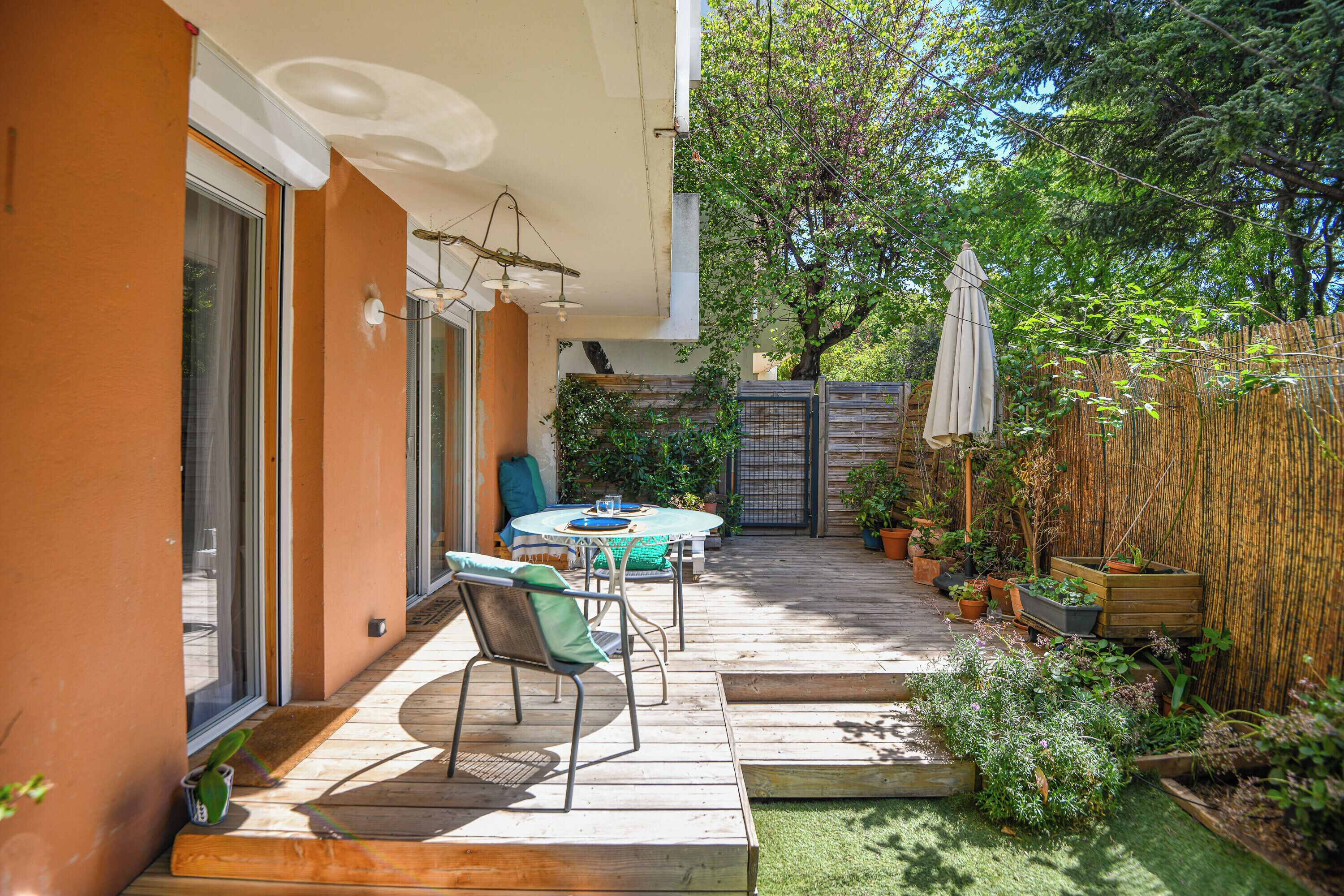 Un patio con mesa y sillas, una terraza de madera y plantas en macetas.