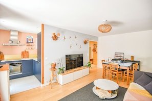 Ein modernes Wohnzimmer mit Fernseher, Sofa, Esstisch und Küchenzeile.