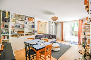 Ein helles Wohnzimmer mit Essbereich, einer Bücherwand, einem Sofa und einem großen Fenster.