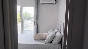 Een slaapkamer met een bed, nachtkastje, raam met gordijnen en een airconditioning.