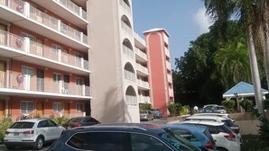 Een meerhoog gebouw met balkons, geparkeerde auto's en palmbomen.