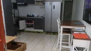 Een compacte keuken met een koelkast, magnetron en een kleine eethoek met een tafel en stoelen.