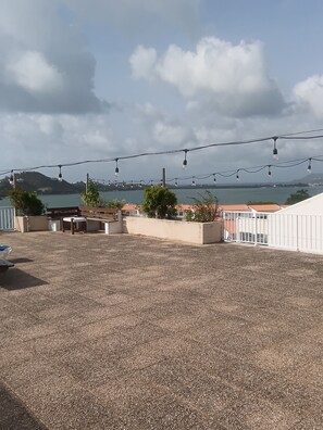 Eine Dachterrasse mit Meerblick, Lichterketten und Gartenmöbeln.
