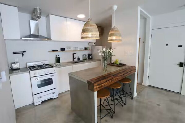 A modern kitchen with white cabinets, a built-in stove, hanging pendant lights, and a wooden island with stools.