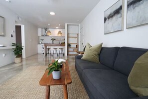 A modern living room with a sofa, a coffee table with a plant, and a kitchen in the background.