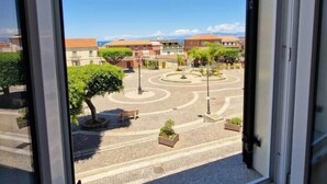 A view through a window of a courtyard with a circular design, buildings in the background, and a clear sky.