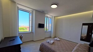 A hotel room with a bed, a desk, a TV, and a large window with a view.