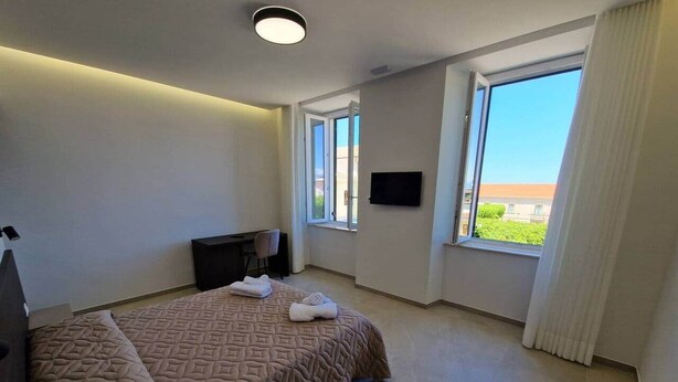 A bedroom with a bed, a desk, a chair, a TV, and a window with a view.