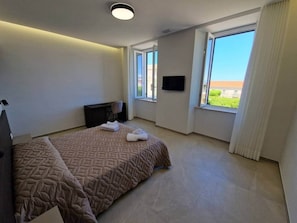 Ein Schlafzimmer mit Bett, Schreibtisch, Stuhl, Fernseher und einem Fenster mit Aussicht.