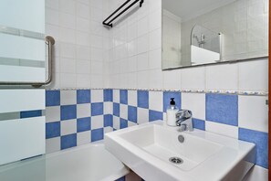 Une salle de bain avec un lavabo blanc, un miroir et des carreaux bleus et blancs formant un motif à carreaux.