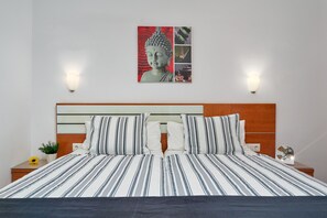Un lit bien fait, avec une literie à rayures, un tableau représentant un Bouddha accroché au mur et deux appliques murales.