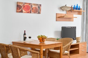 Ein Essbereich mit Holztisch, Korbstühlen, einer Obstschale, Weingläsern und einem Fernseher auf einem Schrank.