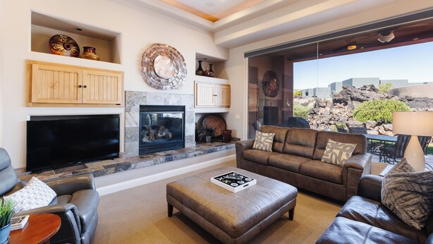 Una sala de estar con chimenea, sofás de cuero, un televisor de pantalla plana y vistas a un paisaje rocoso.