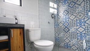 Un baño con inodoro blanco, un mueble de madera y una zona de ducha con azulejos.