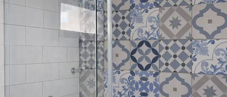 Una ducha con puerta de cristal, inodoro blanco y azulejos estampados.
