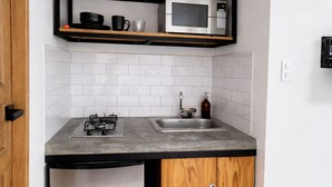 Una cocina compacta con microondas integrado, un lavamanos y un refrigerador pequeño.