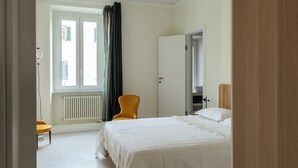 Hotellihuone, jossa on sänky, tuoli, patteri ja ikkuna, jossa on verhot.