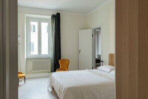 Ein Hotelzimmer mit Bett, Sessel, Heizkörper und einem Fenster mit Vorhängen.