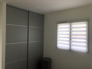 A room with a sliding door, a window with blinds, and a small trash bin. - Summer rental Porto-Vecchio (Porto vecchio)