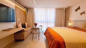 Quarto de hotel com cama, televisão, secretária com cadeira e janela com cortinas.