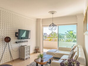 Ein modernes Wohnzimmer mit Fernseher, Sofa, Couchtisch und einem Balkon mit Blick.